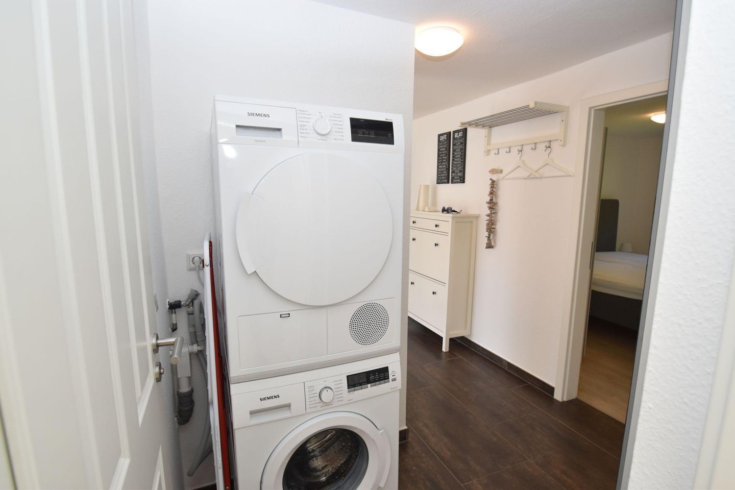 Un lavadero con lavadora y secadora apiladas, un armario blanco y un espejo en la habitación contigua.