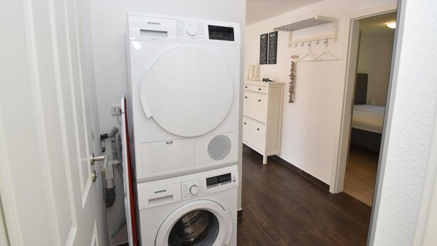 Un lavadero con lavadora y secadora apiladas, un armario blanco y un espejo en la habitación contigua.
