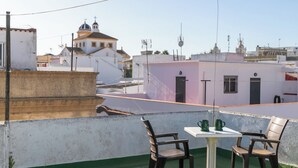 A rooftop terrace with a table and chairs, a view of buildings, and a clear sky.