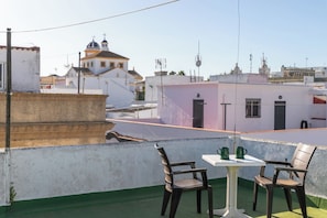 A rooftop terrace with a table and chairs, a view of buildings, and a clear sky.