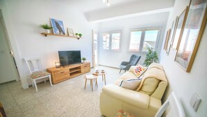 A living room with a sofa, TV, wooden entertainment unit, and a small table.