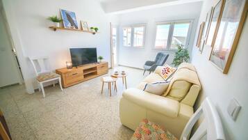 Una sala de estar con sofá, televisión, mueble de entretenimiento de madera y una mesita.