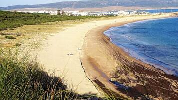 Un paysage côtier avec une plage de sable, des dunes herbeuses et une ville située au loin.