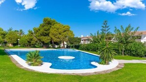 A swimming pool surrounded by well-maintained grass and trees, with a clear blue sky in the background. - Top Apartment with Sea View and Pool (el Gran Alacant)