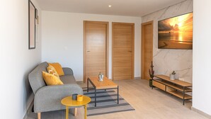A modern living room with a grey sofa, wooden doors, a coffee table, and a large painting of a sunset. - Top Apartment with Sea View and Pool (el Gran Alacant)