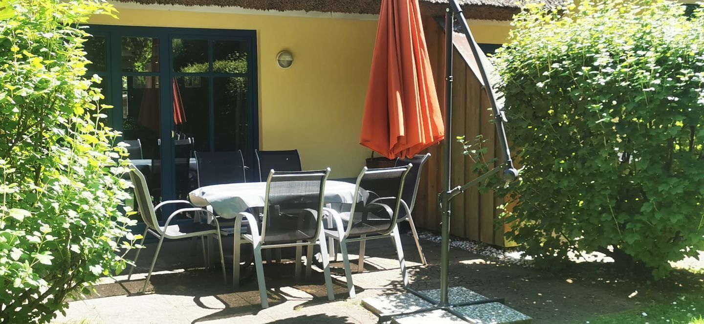 Un patio al aire libre con una mesa y sillas, una sombrilla cubierta y una valla de madera.
