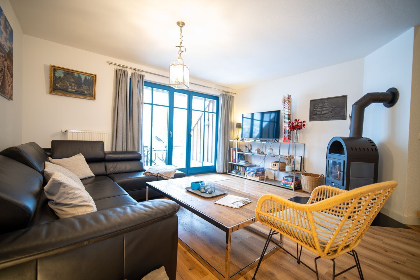 A cozy living room with a sofa, a coffee table, a wicker chair, a TV stand, and a wood-burning stove.