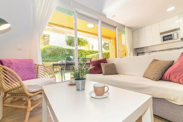 Un salón acogedor con un sofá, un sillón de mimbre, una mesa de centro y vistas al exterior.