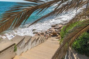 Una escalera de hormigón que baja hacia una playa rocosa y las olas del océano.