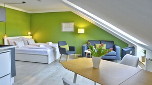 A modern, well-lit room with a bed, a sofa, a dining table, and a chair. - fewo1846 - Beach shell (App. 638) / Studio apartment with sea view on the 3rd floor - (Harrislee)