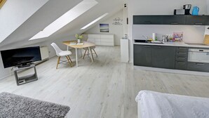A modern loft apartment with a dining area, kitchenette, and a TV mounted on the wall. - fewo1846 - Beach shell (App. 638) / Studio apartment with sea view on the 3rd floor - (Harrislee)