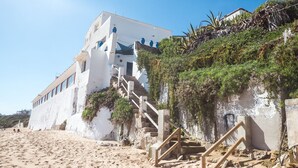 A white building with a staircase leading to a beach area.