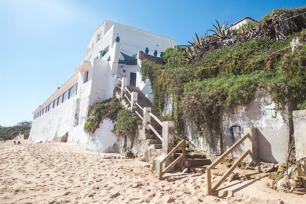 A white building with a staircase leading to a beach area.