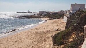 A beach with buildings along the shore, a lighthouse in the distance, and rocky terrain.
