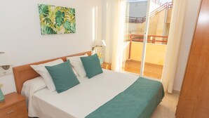 A bedroom with a bed, a nightstand, a lamp, a painting, and a view of a balcony.