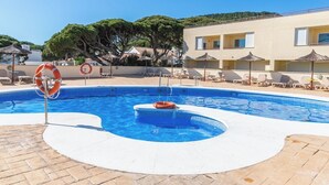 A swimming pool with lounge chairs and umbrellas, surrounded by a building with a tiled roof.