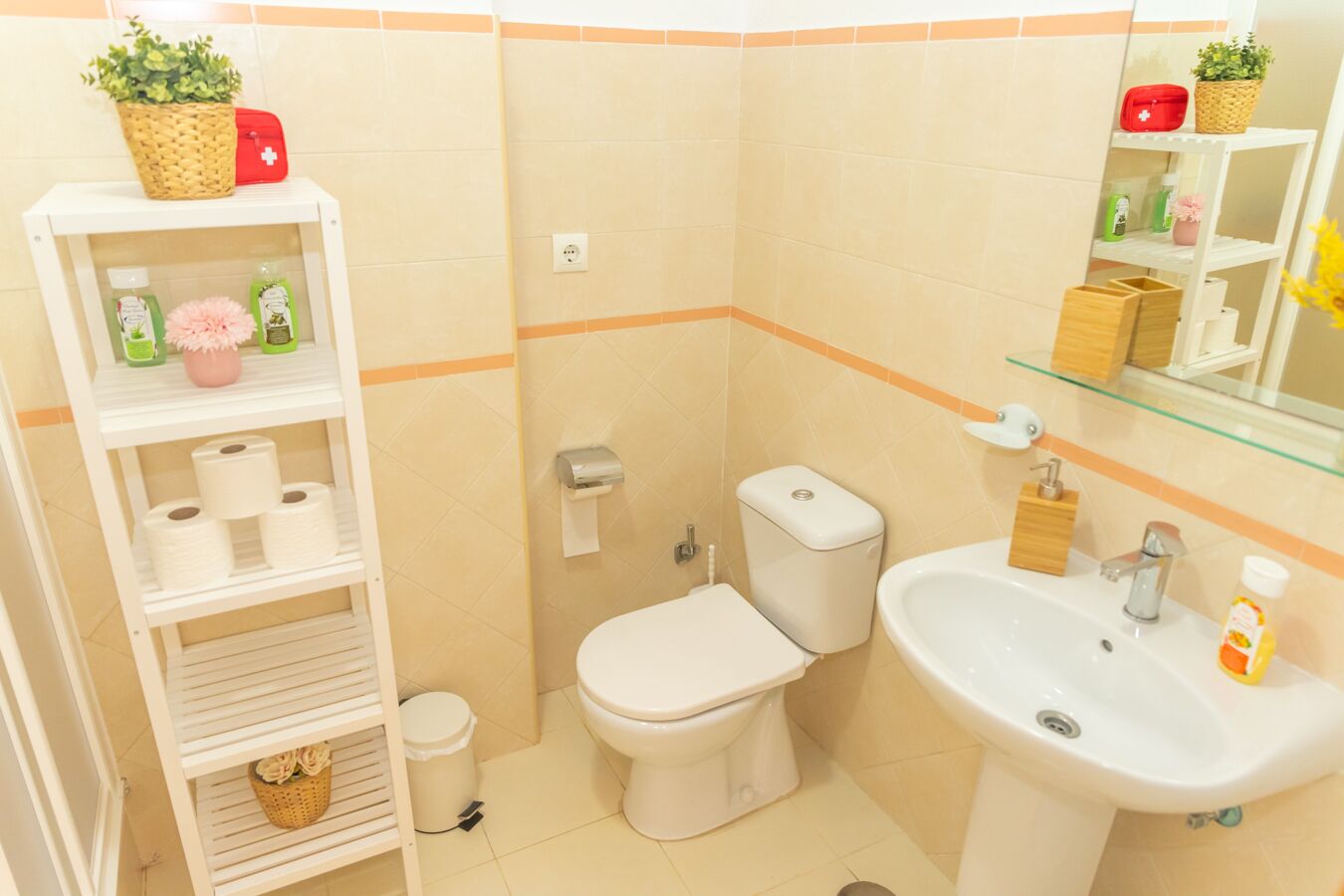 Un baño pequeño con inodoro, lavamanos y repisas con artículos de aseo.