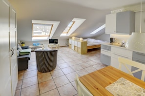 A compact, modern apartment with a kitchen, dining area, and a small living space. There are skylights providing natural light, a TV, and a small table with chairs.