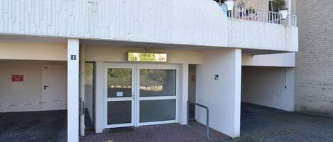 Une entrée d’immeuble avec une plaque indiquant « HAUS 4 628 641 », une entrée fermée par un portail et un petit jardinier.