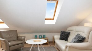 A modern living room with a high ceiling, a skylight, a beige sofa, a white coffee table, and a grey rug. - fewo1846 - Little Mermaid (App. 666) / Studio apartment on the top floor - (Harrislee)