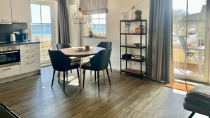 A modern kitchen with a dining area, large windows with curtains, and a view of the sea. - fewo1846 - KüstenNest (App. 590) / Studio apartment with 2 balconies on the 1st floor - (Harrislee)