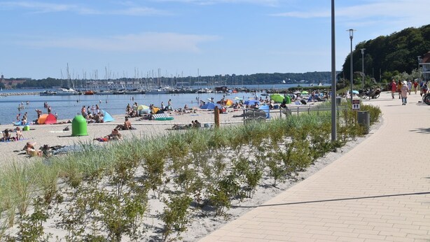 A beach with people sunbathing and swimming, a marina with boats, and a paved walkway with street lamps. - fewo1846 - KüstenNest (App. 590) / Studio apartment with 2 balconies on the 1st floor - (Harrislee)