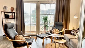 A modern living room with a sofa, two armchairs, a coffee table, and a bookshelf. - fewo1846 - KüstenNest (App. 590) / Studio apartment with 2 balconies on the 1st floor - (Harrislee)