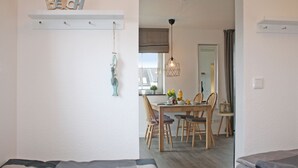 A room with a bed, a dining area with a table and chairs, a hanging light fixture, and a wall-mounted shelf with decorative items. - fewo1846 - KüstenNest (App. 590) / Studio apartment with 2 balconies on the 1st floor - (Harrislee)