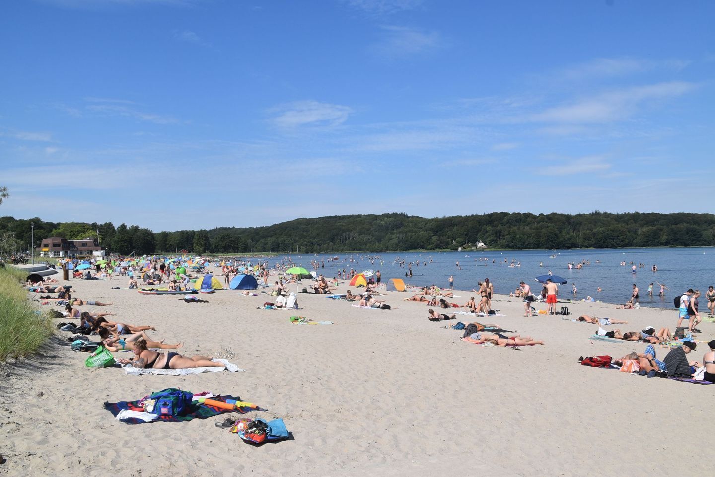 En overfyldt strand med folk, der solbader og svømmer.