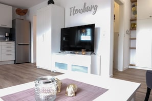A modern kitchen with a built-in TV, white cabinetry, and a dining area with a table and decorative items.