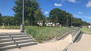 A paved pathway with metal railings, leading to a sandy area with steps. - fewo1846 - MuschelNest (App. 621) / Studio apartment with balcony on the 2nd floor - (Harrislee)
