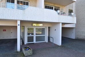 Une entrée d’immeuble avec une plaque indiquant « HAUS 4 628 641 », une entrée fermée par un portail et un petit jardinier.