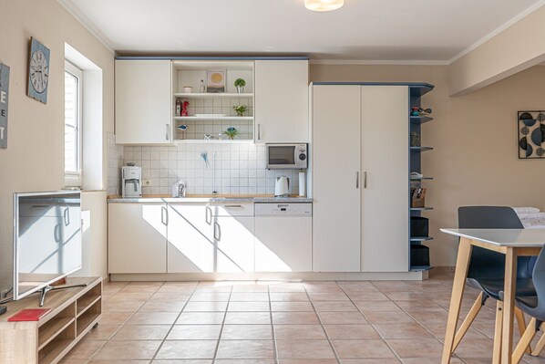 A compact kitchen with white cabinets, a microwave, and a coffee machine. There is a small dining area with a table and chairs. - fewo1846 - Fördeblick II (Apartment 671) Studio apartment with a terrace on the mezzanine level (Harrislee)
