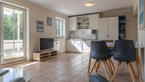 A modern kitchen with white cabinets, a built-in microwave, and a dining area with two black chairs and a small table. - fewo1846 - Fördeblick II (Apartment 671) Studio apartment with a terrace on the mezzanine level (Harrislee)