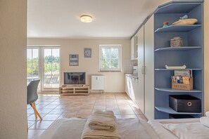 A modern living room with a TV, a sofa, a dining table, and a kitchen area with cabinets and a refrigerator.
