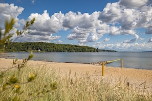 A beach with a volleyball net, a sandy shore, and a forested hill in the background. - fewo1846 - Fördeblick II (Apartment 671) Studio apartment with a terrace on the mezzanine level (Harrislee)