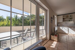 Une cuisine moderne avec des meubles blancs, un coin repas comprenant une table et des chaises, et de grandes fenêtres offrant une vue sur les arbres et un ciel dégagé.