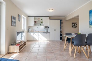 A modern kitchen with white cabinets, a microwave, and a coffee machine. There is a dining area with a table and chairs.