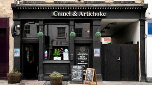 A black storefront with the sign "Camel & Artichoke" and a signboard advertising daily deals. - Open plan Waterloo, 2BR, New build, terrace, by Blueground (London)