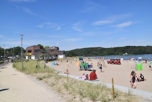 Une plage avec un bâtiment, un sentier sablonneux et une étendue d’eau.