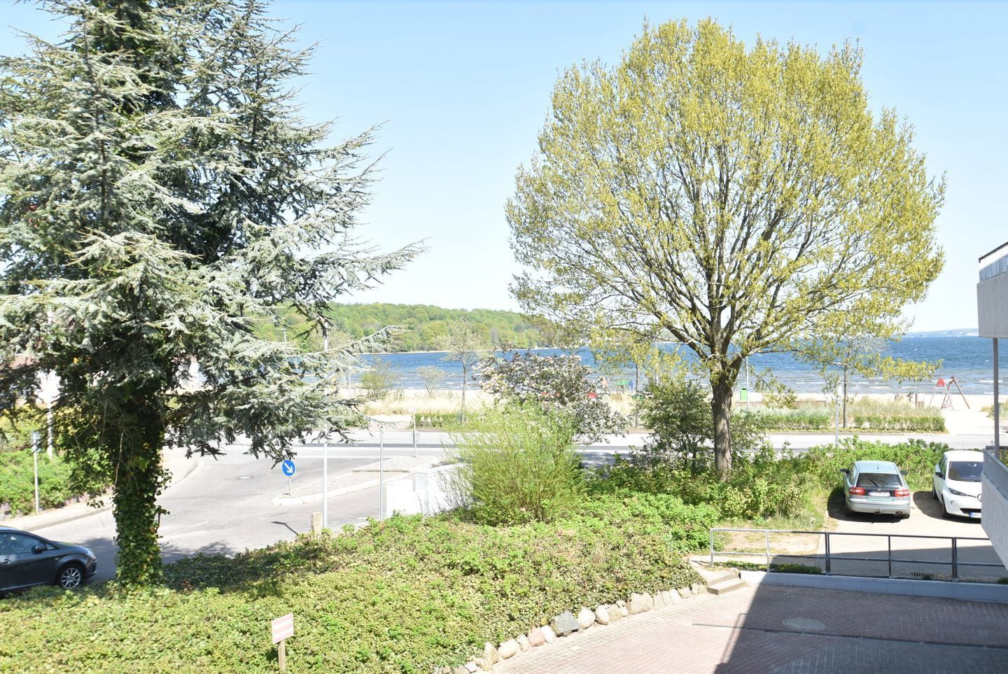 Un espace de stationnement avec des voitures, une route et une vue sur une étendue d’eau et de la végétation.