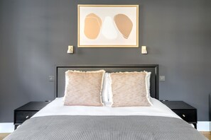 A bedroom with a large bed, two bedside tables, a framed artwork above the bed, and a gray wall. - Open plan Waterloo, 1BR, New build, terrace, by Blueground (London)