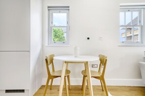 A room with a round wooden table and two chairs, a white vase on the table, and two windows with white frames. - Open plan Waterloo, 1BR, New build, terrace, by Blueground (London)