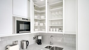 A modern kitchen with white cabinets, a Bosch toaster, a LaMenta microwave, a coffee maker, and a sink. - Open plan Waterloo, 1BR, New build, terrace, by Blueground (London)