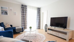 Una sala moderna con un sofá azul, una mesa de centro redonda, un televisor de pantalla plana sobre un soporte de madera y una alfombra estampada.