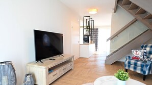 Una sala de estar moderna con un televisor de pantalla plana sobre un soporte de madera, una mesita con una planta y un sillón azul de pata de gallo con un cojín.