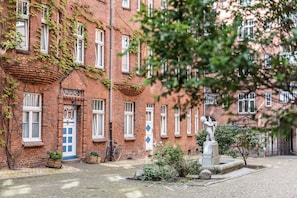 A brick building with a blue door, a bicycle, and a statue in the courtyard.