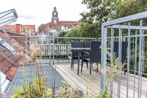 Eine Dachterrasse mit Sitzgelegenheiten im Freien, einem Metallgeländer und Blick auf ein historisches Gebäude mit einem Turm.