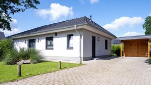 A single-story building with a tiled roof, a paved driveway, and a wooden garage door. - Ferienhaus Anker - Ferienhaus Anker auf Rügen (Garz/Rügen)