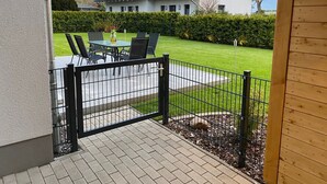 A patio area with a table and chairs, a black metal fence, and a well-maintained lawn. - Ferienhaus Anker - Ferienhaus Anker auf Rügen (Garz/Rügen)